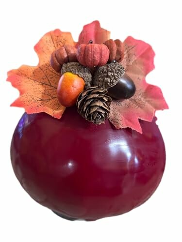 Red apple with autumn leaves and pinecone decoration on top.